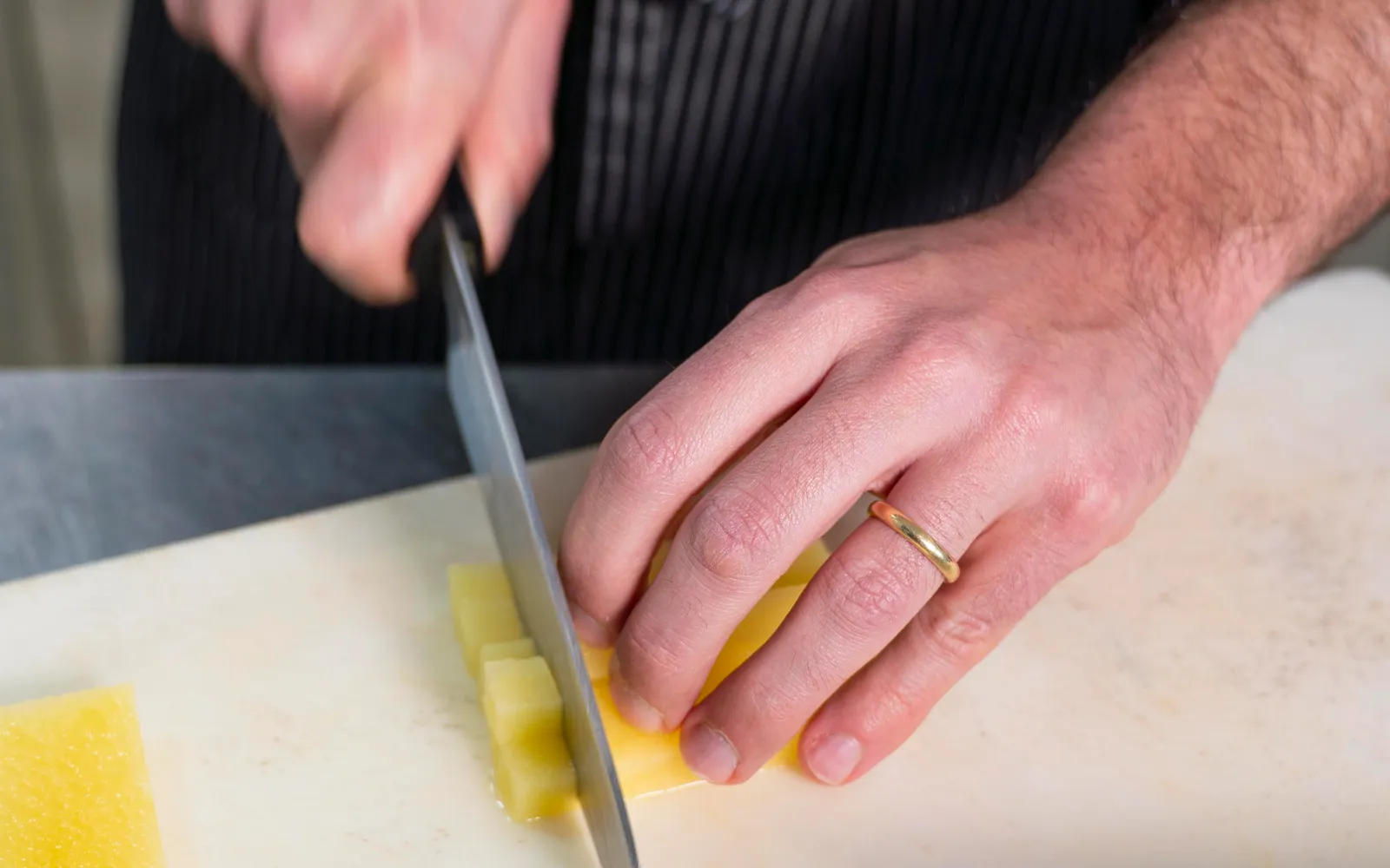 Le mani di uno chef che tagliano un ingrediente sul tagliere in cucina
