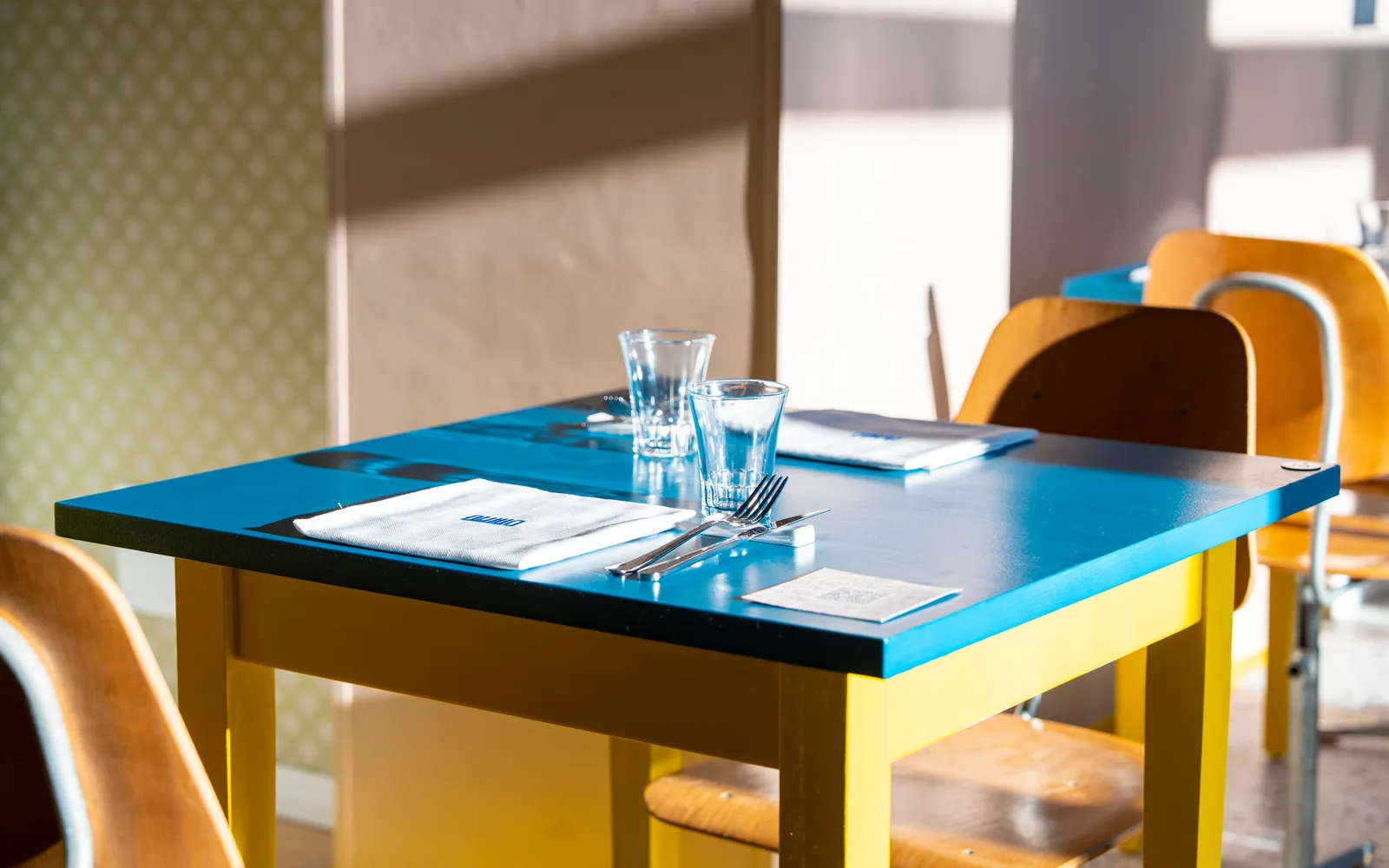 Tavolo apparecchiato di Duilio con piano blu, bicchieri e luce naturale